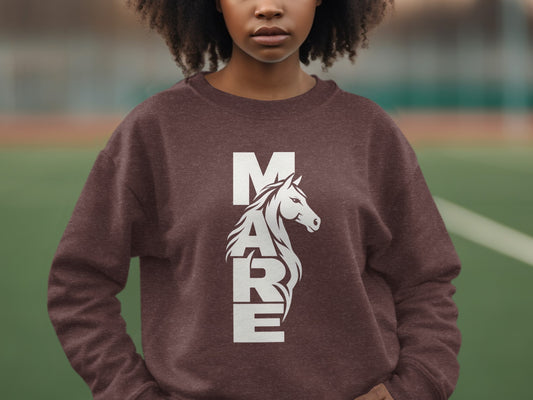 A person wearing a brown sweatshirt with white graphic text spelling MARE and a horse head.