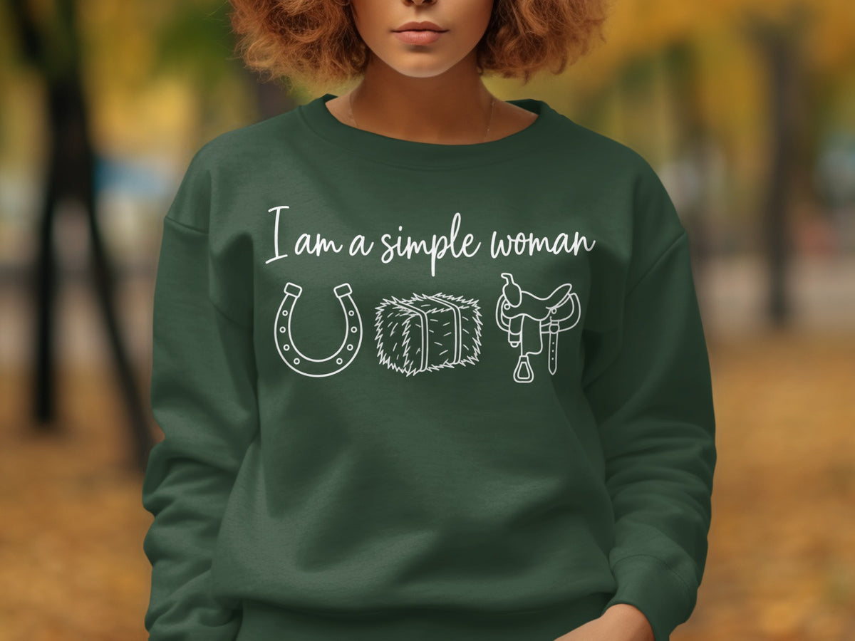 Green sweatshirt with white text "I am a simple woman" above a horseshoe, hay bale, and saddle.