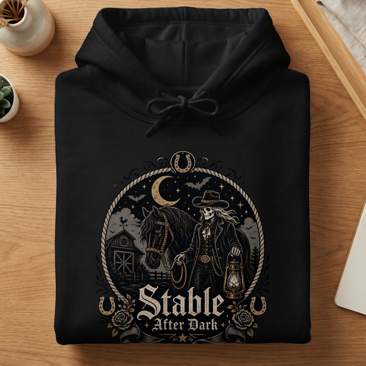 Black hoodie with a graphic of a skeletal cowboy, horse, barn, and text "Stable After Dark".