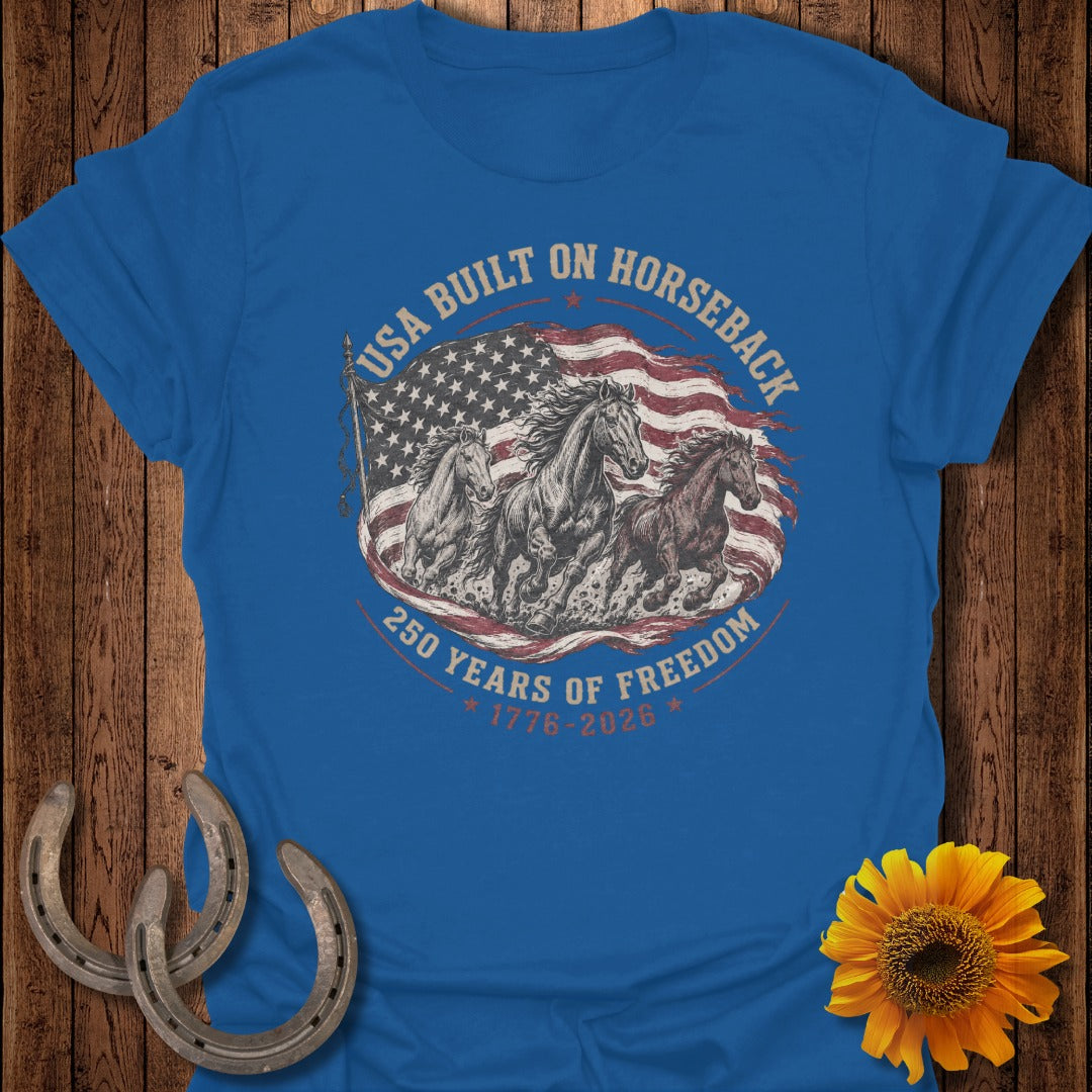 Blue t-shirt with horses running before the US flag, reads "USA Built on Horseback, 250 Years of Freedom."
