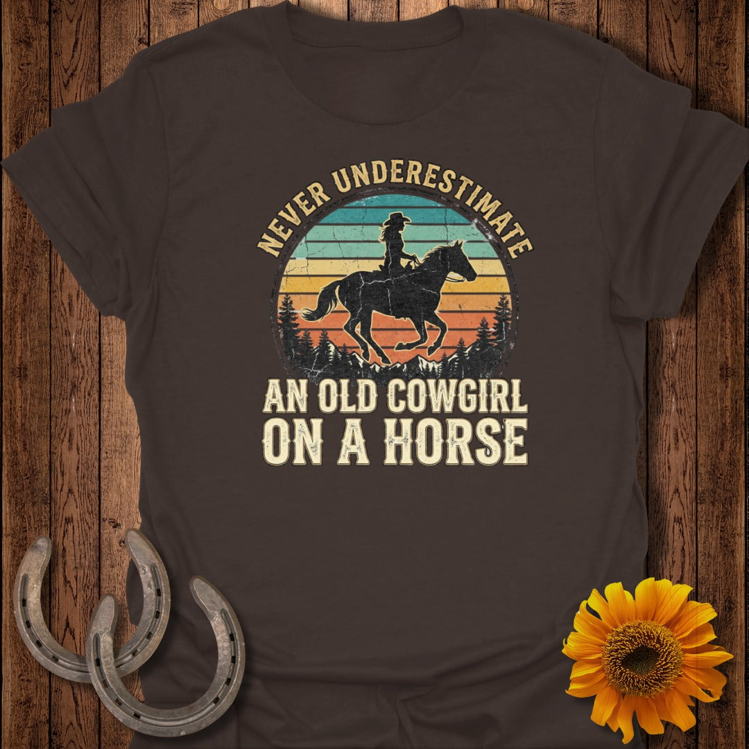 Vintage sunset with cowboy silhouette and text "Never Underestimate An Old Cowgirl On A Horse".