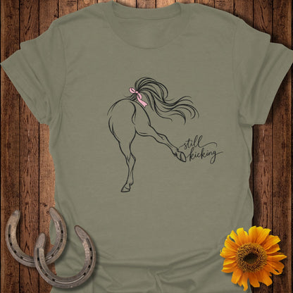 T-shirt with a line drawing of a horse kicking, a pink ribbon in its tail, and "still kicking" text.