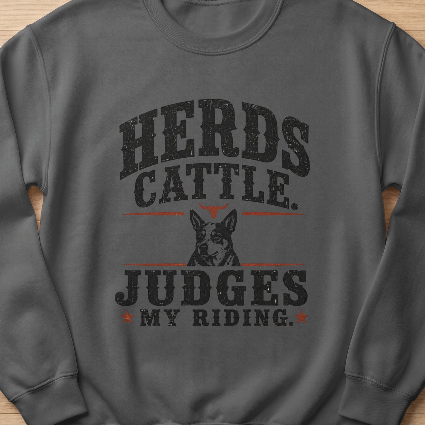 Grey sweatshirt with "Herds Cattle. Judges My Riding." text and dog graphic.
