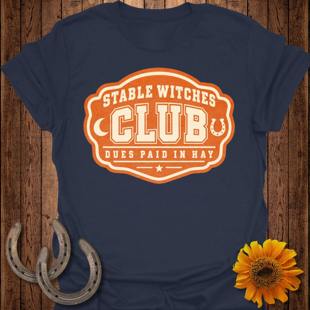 Navy t-shirt with orange and cream "Stable Witches Club" graphic.