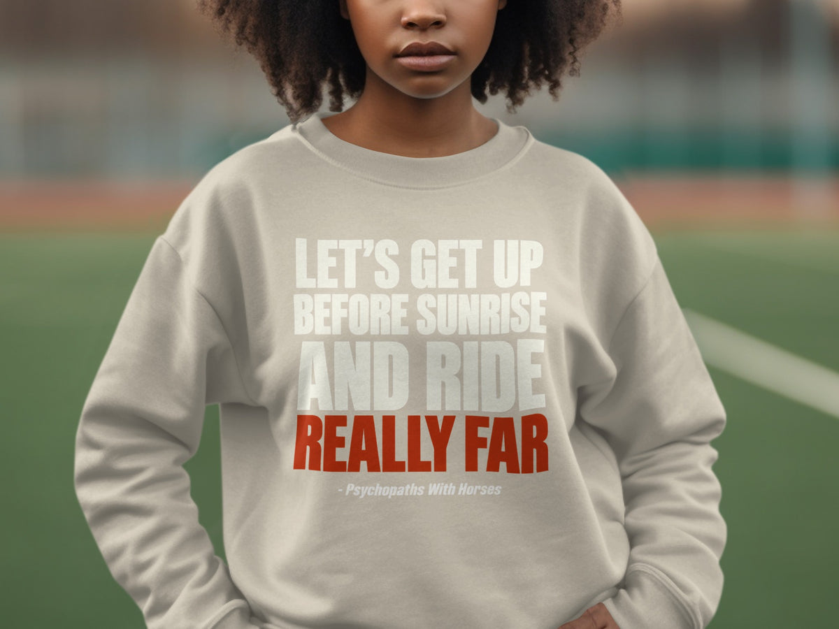 A person wearing a beige sweatshirt with white and red text stating, Let's get up before sunrise and ride really far.