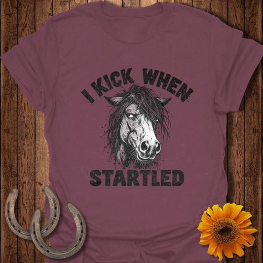 A maroon t-shirt featuring a distressed black graphic of a horse's head and the text "I KICK WHEN STARTLED".
