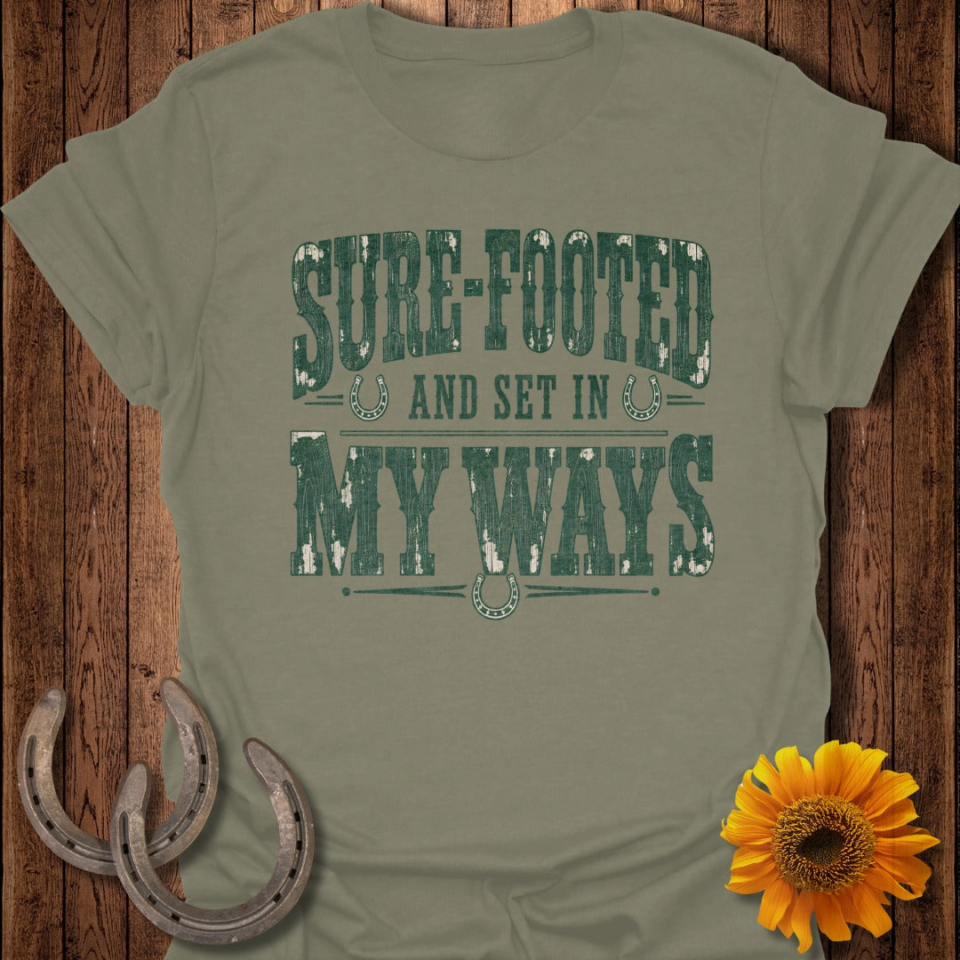 Olive green t-shirt with distressed "Sure-Footed And Set In My Ways" text and horseshoes.