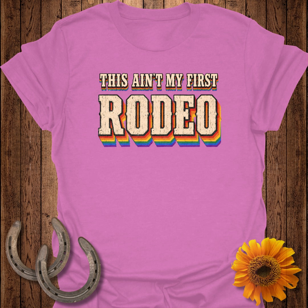 Pink t-shirt with "THIS AIN'T MY FIRST RODEO" in rainbow lettering.