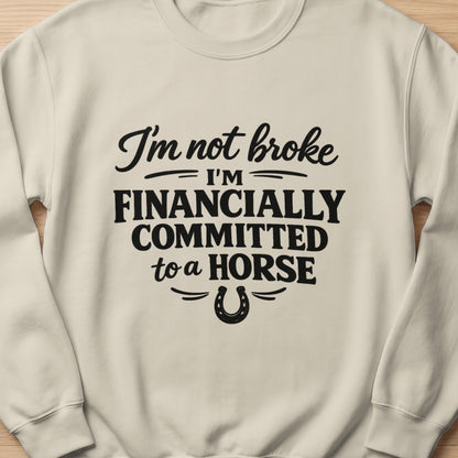 Cream sweatshirt with black text and horseshoe graphic reading "I'm not broke I'm financially committed to a horse."