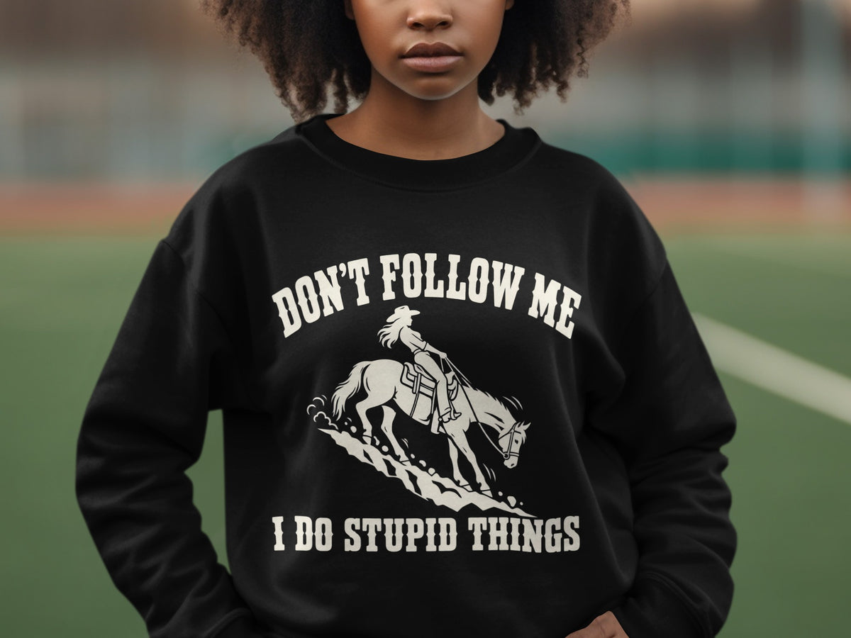 A person wearing a black sweatshirt with white text reading DON'T FOLLOW ME I DO STUPID THINGS and an illustration of a person riding a horse.