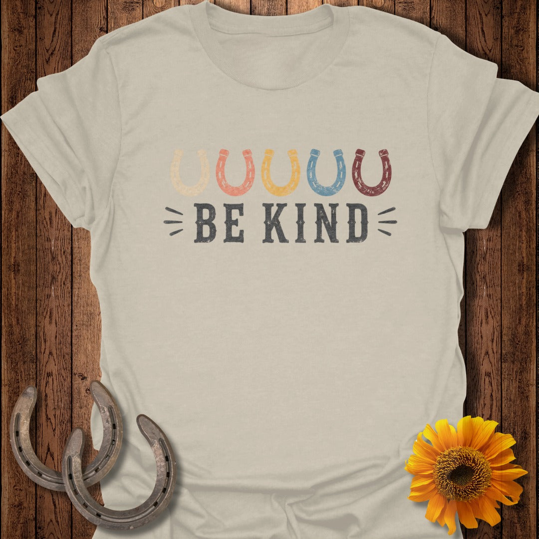 Be Kind text with colorful horse shoes on a beige t-shirt.