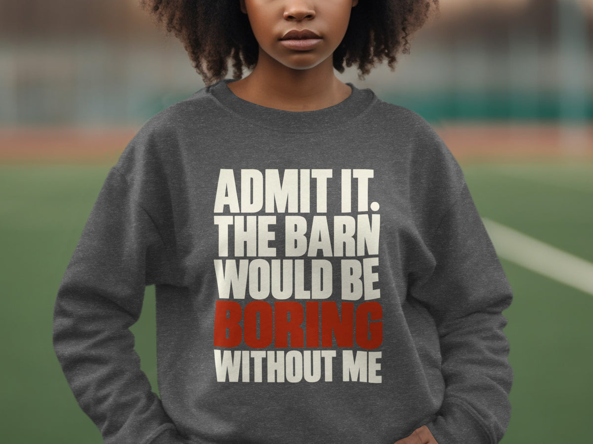 A person wearing a dark grey crewneck sweatshirt featuring white and red text stating admit it the barn would be boring without me.