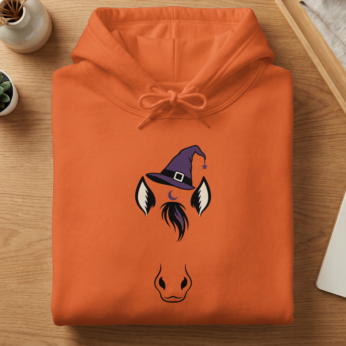 Orange hoodie with a witch hat and horse face graphic.