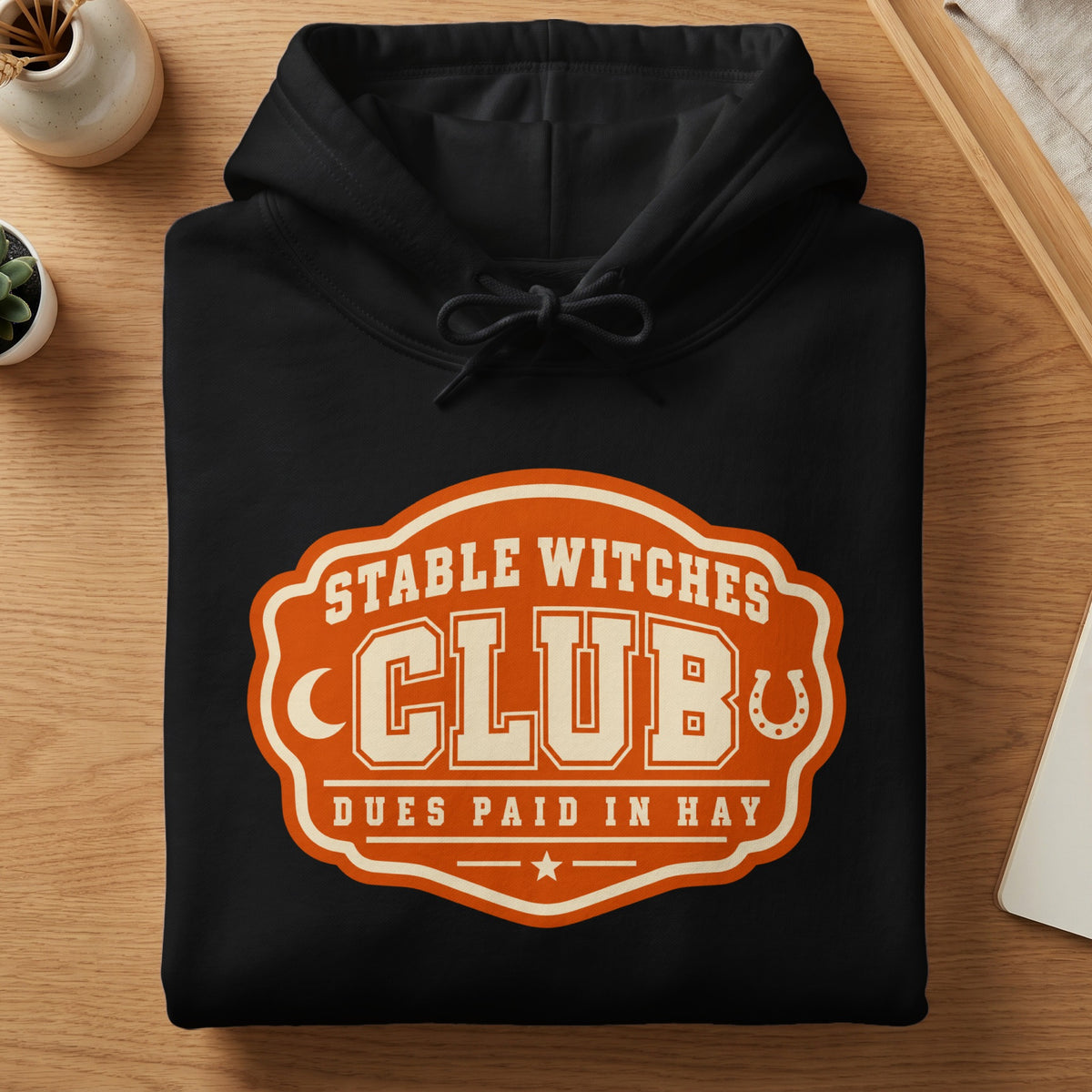 Black hoodie with an orange and cream "Stable Witches Club" logo featuring a horseshoe.