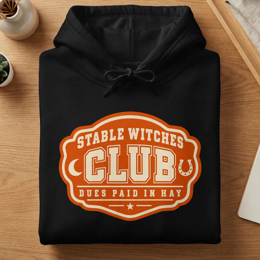 Black hoodie with an orange and cream "Stable Witches Club" logo featuring a horseshoe.