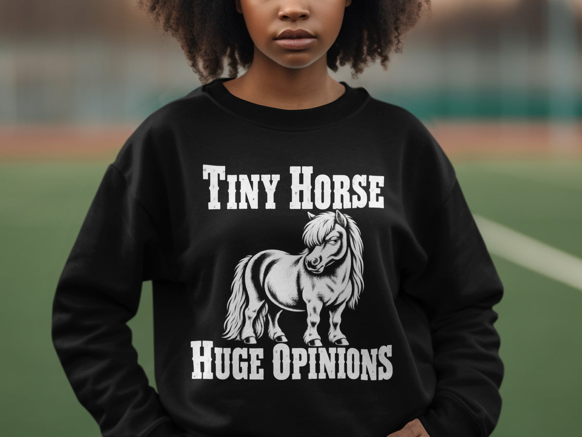 A person wearing a black sweatshirt printed with white text reading Tiny Horse Huge Opinions above and below a pony illustration.