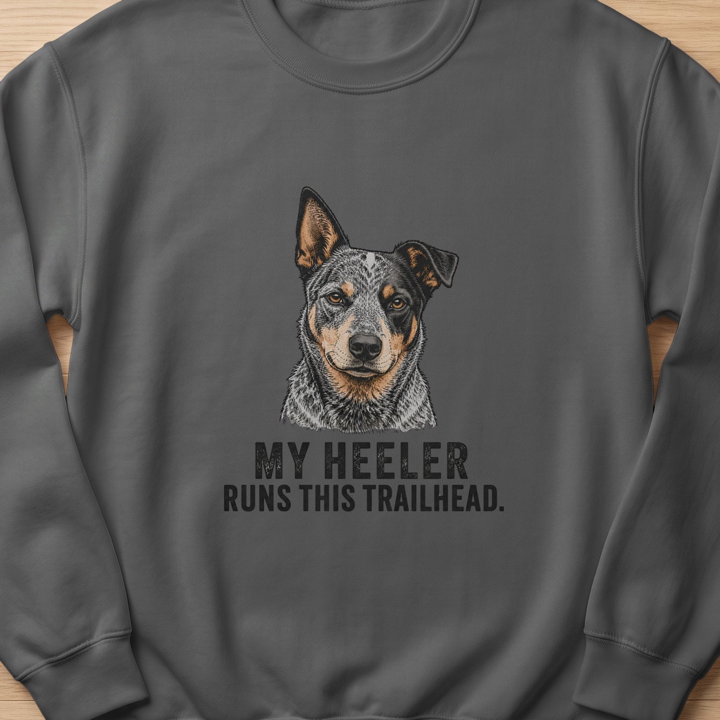 Dark grey sweatshirt with an illustration of a cattle dog and text that reads "My Heeler Runs This Trailhead."