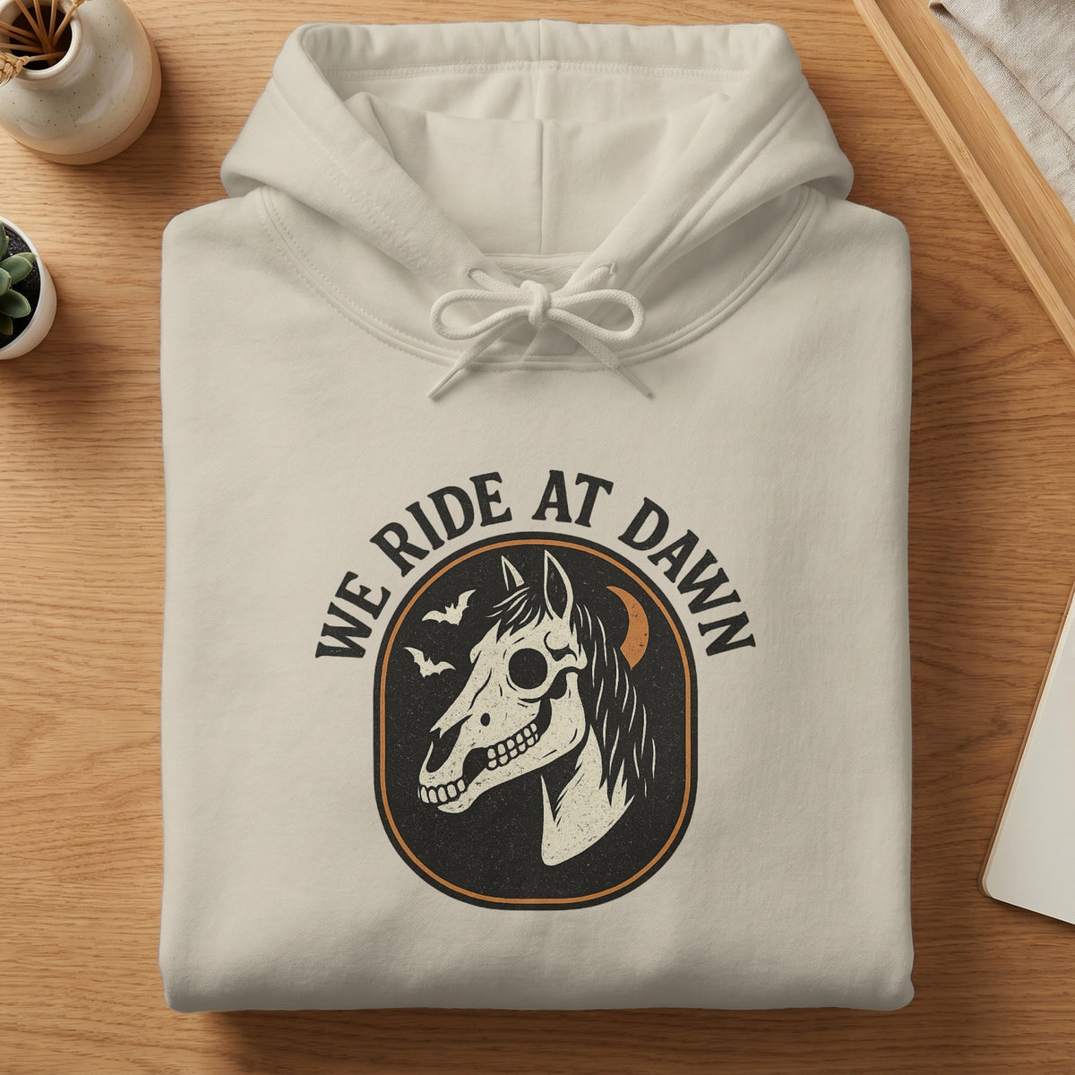 Cream hoodie with a skull horse graphic and "WE RIDE AT DAWN" text.