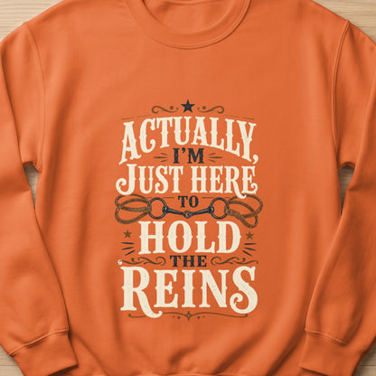 Orange sweatshirt with text "Actually, I'm Just Here to Hold the Reins" and horse bit graphic.