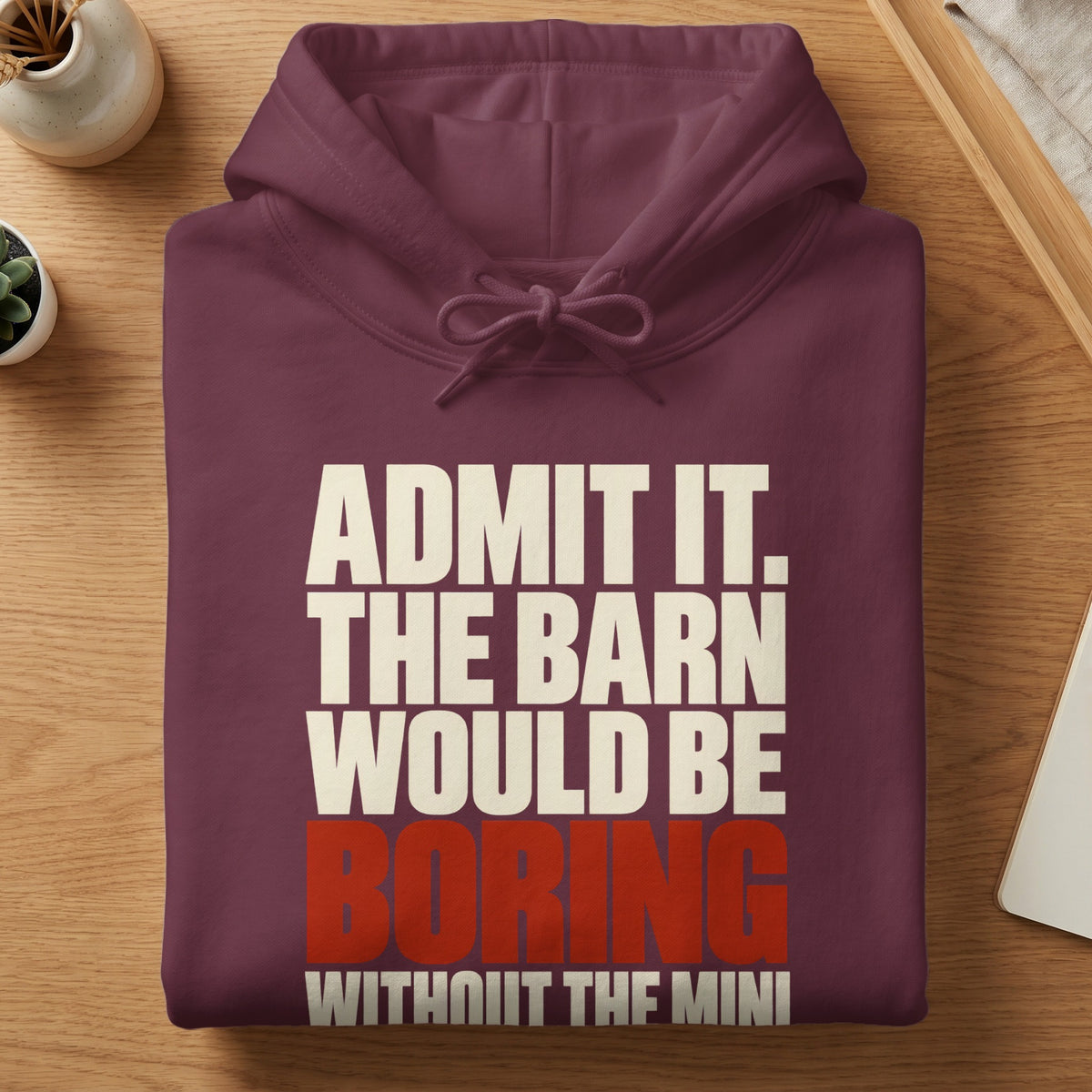 Folded maroon hooded sweatshirt featuring white and red text that reads, Admit it. The barn would be boring without the mini.