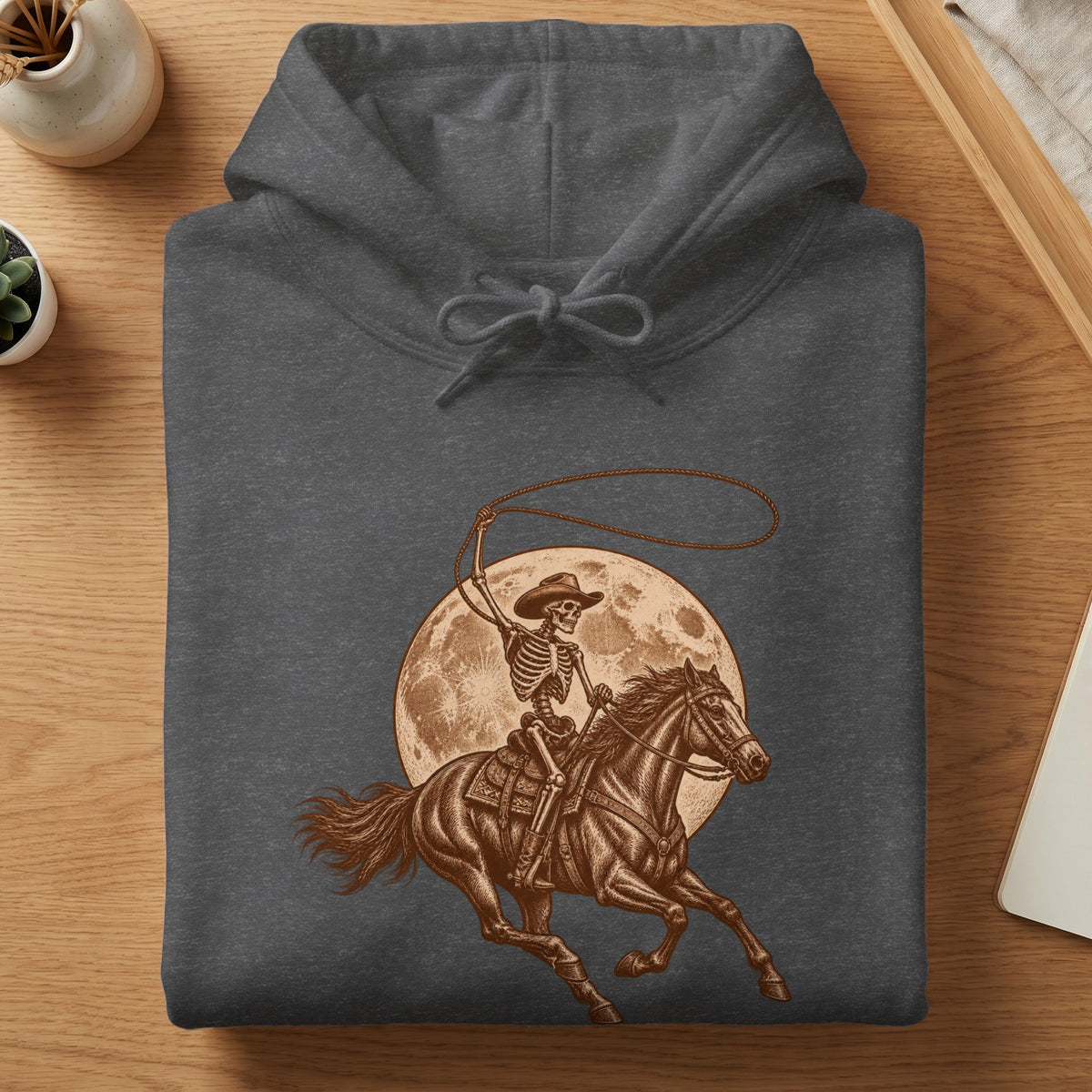 Skeleton cowboy on horseback with a lasso in front of a moon, printed on a gray hoodie.
