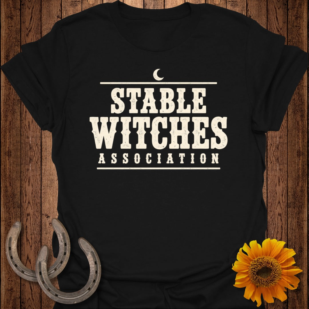 Black t-shirt with "Stable Witches Association" text, horseshoes, and sunflower.
