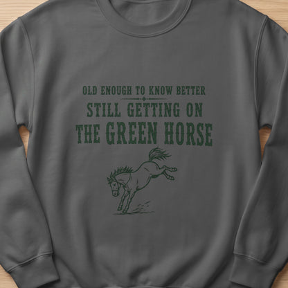 Dark grey sweatshirt with green text and horse graphic: "Old enough to know better still getting on the green horse."
