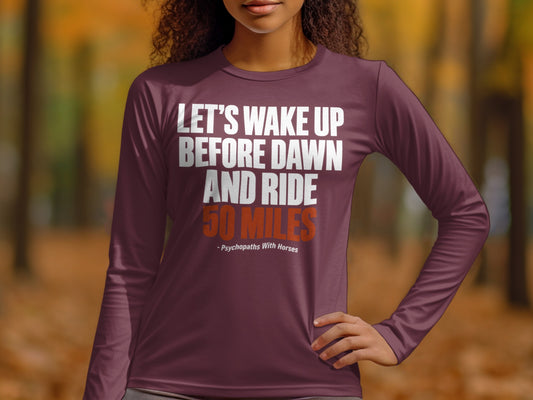 A person wearing a maroon long-sleeve shirt with white and orange text reading Let's wake up before dawn and ride 50 miles.