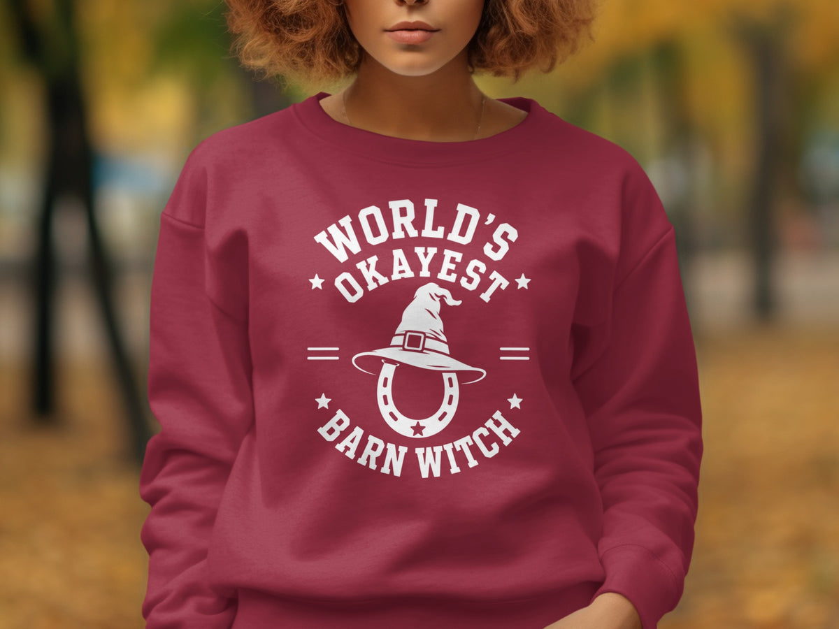 Maroon sweatshirt with white text "World's Okayest Barn Witch" and horseshoe with witch hat graphic.
