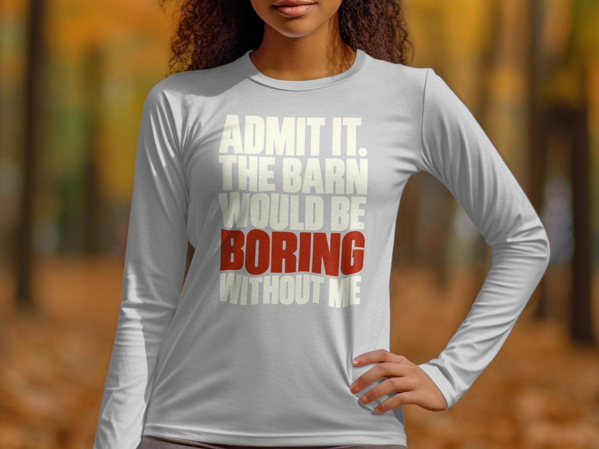 A person wearing a grey long-sleeve shirt with white and red text stating admit it the barn would be boring without me.
