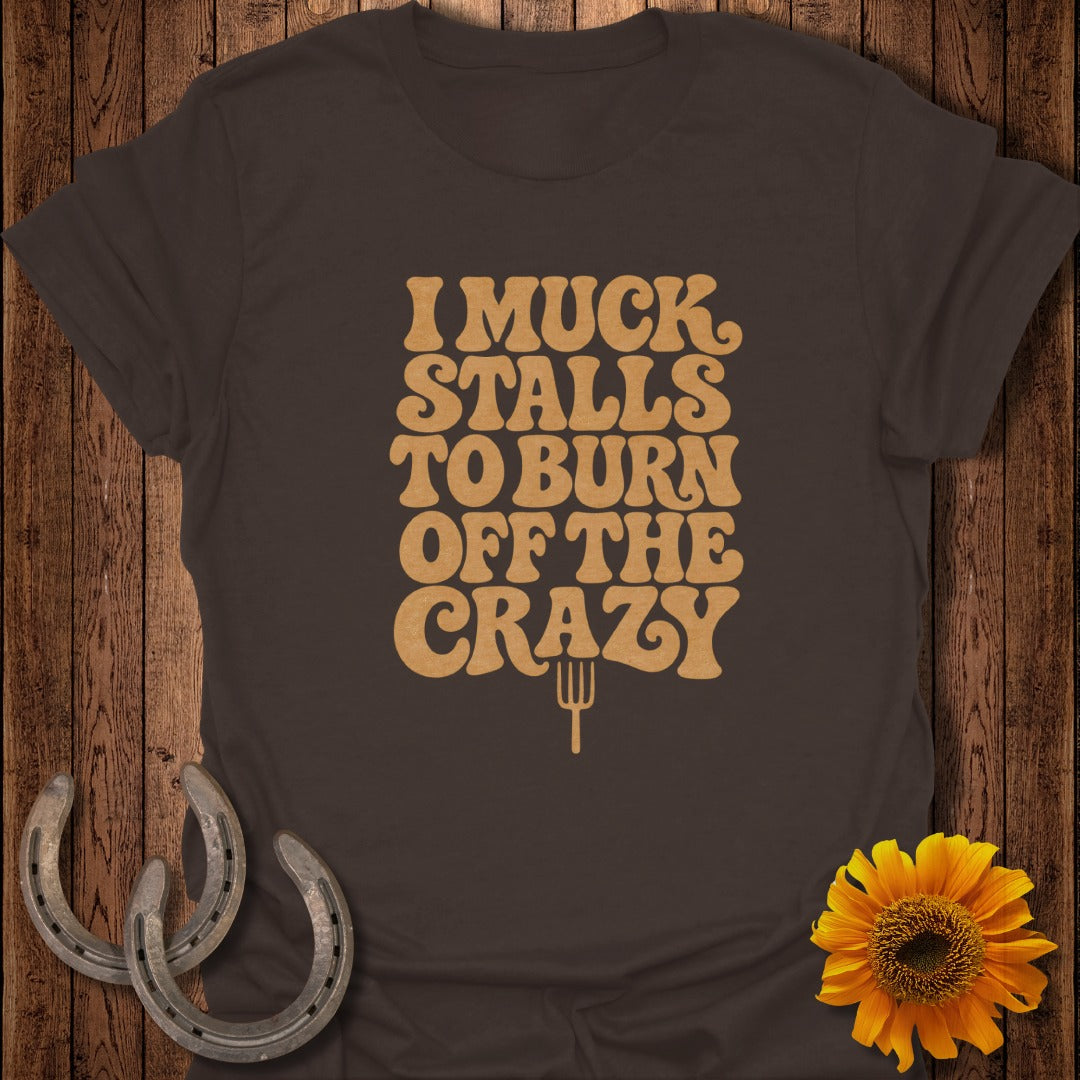 Dark brown t-shirt featuring distressed gold text that reads "I muck stalls to burn off the crazy."