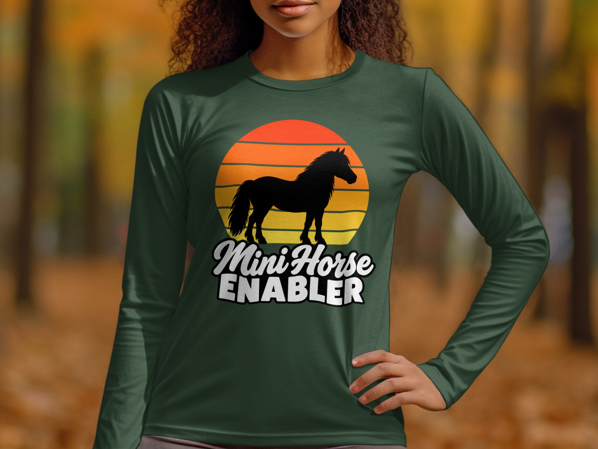 A person wearing a dark green long-sleeve shirt featuring a sunset graphic and the text Mini Horse Enabler.