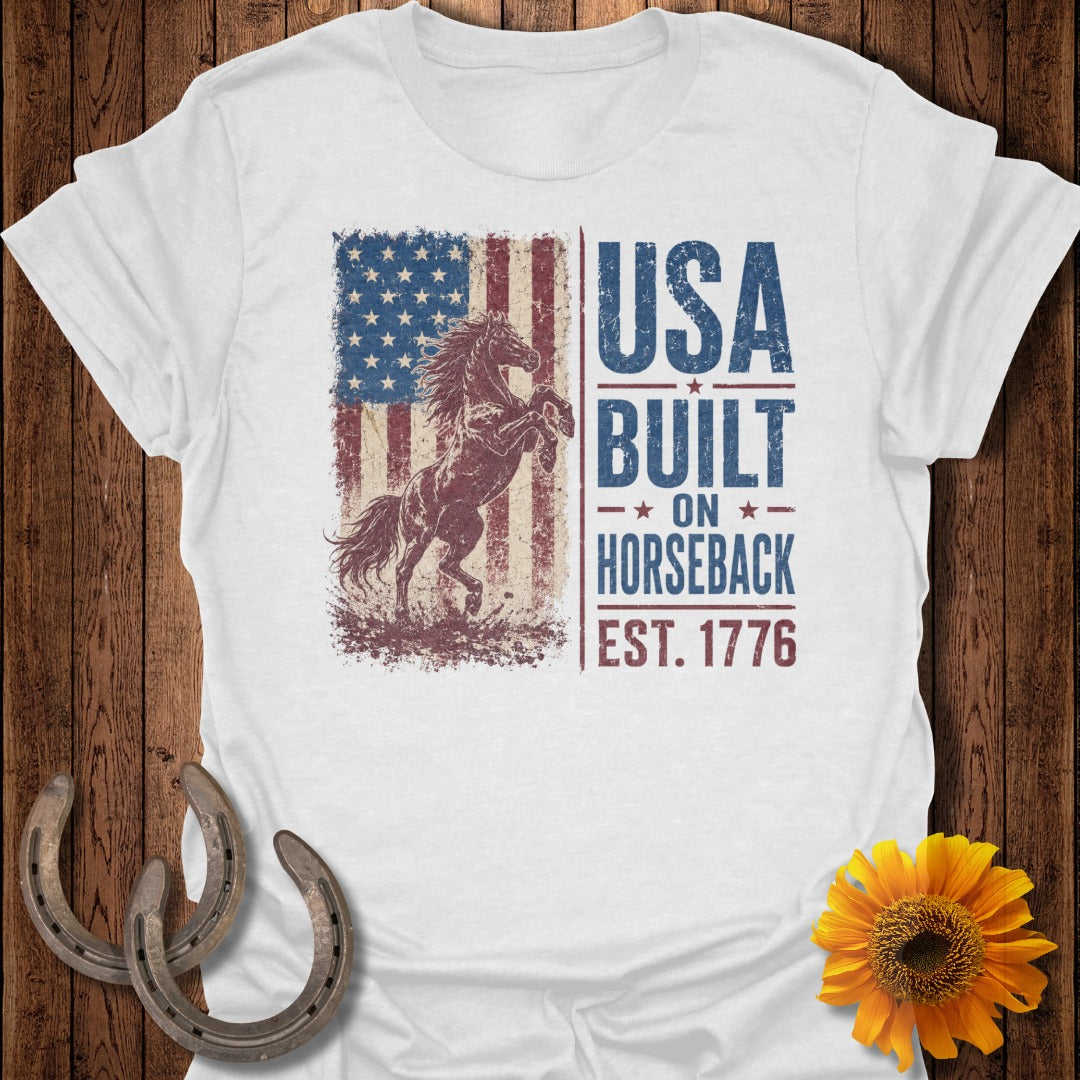 White t-shirt with vintage American flag, rearing horse, and text "USA BUILT ON HORSEBACK EST. 1776".
