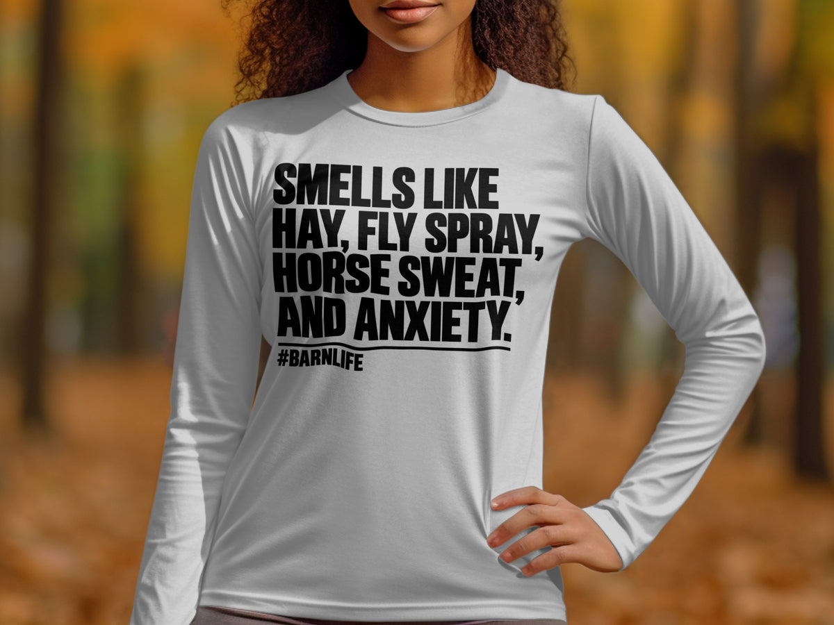 White long sleeve shirt with black text "Smells like hay, fly spray, horse sweat, and anxiety. #barnlife"