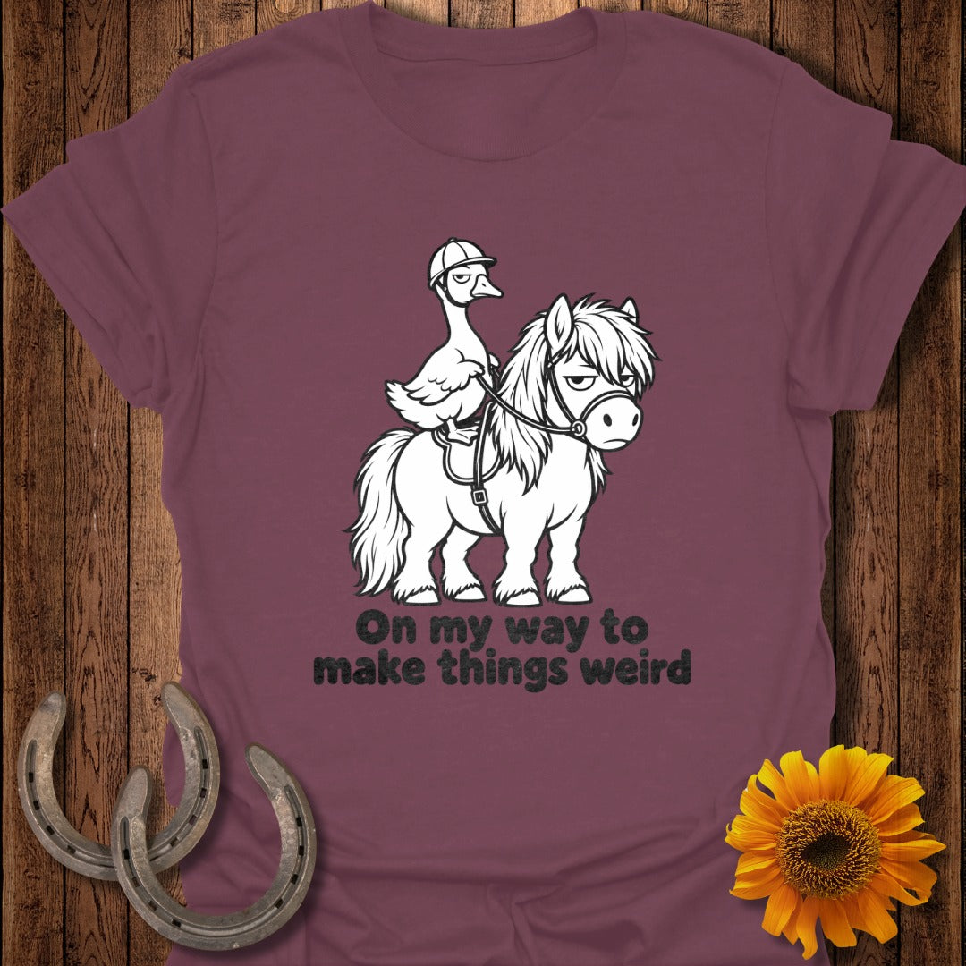 A maroon t-shirt featuring a graphic of a duck wearing a riding helmet on a pony, with the text "On my way to make things weird".
