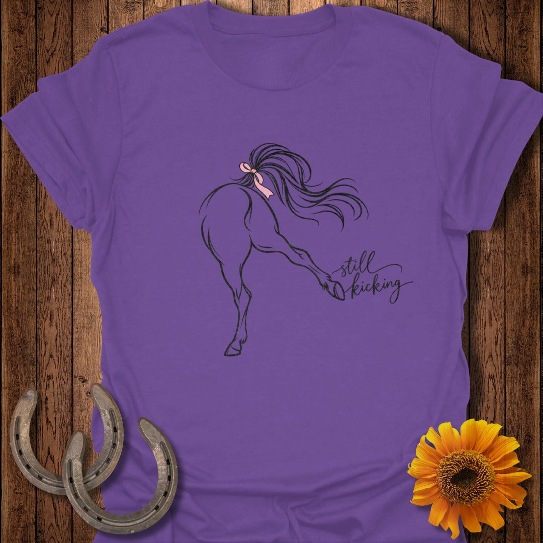Purple t-shirt with black line drawing of a horse kicking and "still kicking" text.