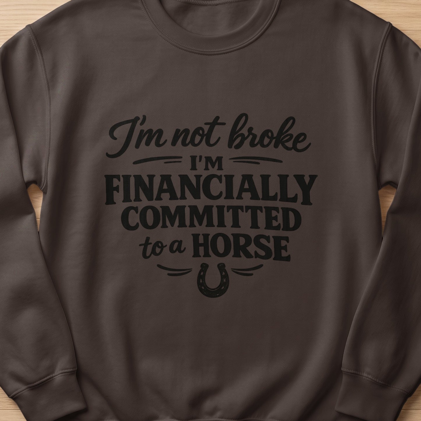 Brown sweatshirt with black text that reads "I'm not broke I'm FINANCIALLY COMMITTED to a HORSE" and a horseshoe.