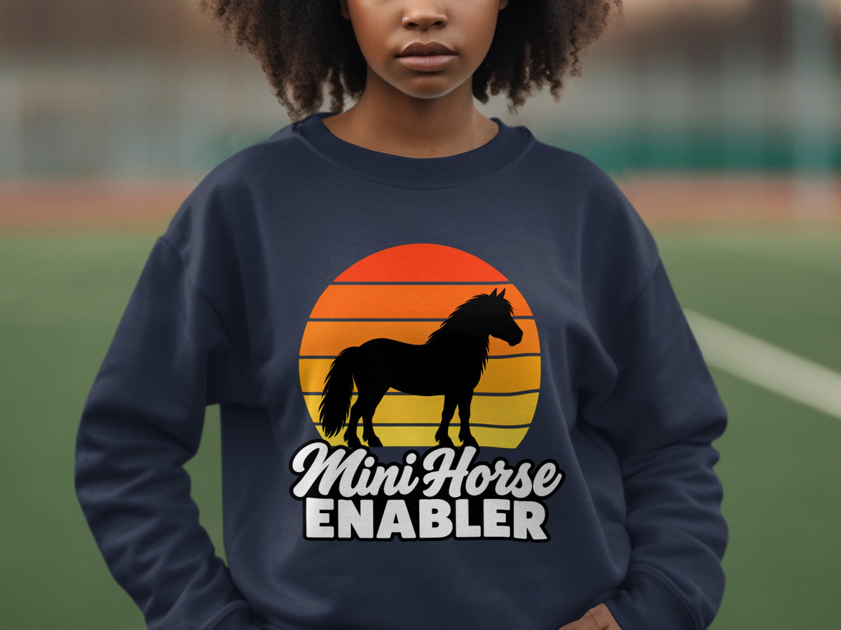 A person wearing a dark blue sweatshirt with a retro sunset horse graphic and the text Mini Horse ENABLER.