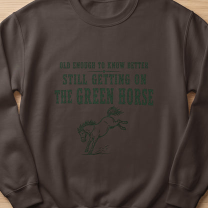 Brown sweatshirt with green text "Old enough to know better, still getting on the green horse" and a horse graphic.