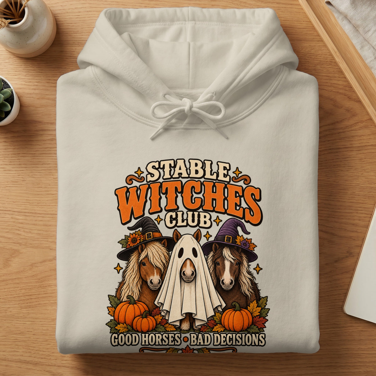 Cream hoodie with "Stable Witches Club" graphic featuring horses, pumpkins, and witches' hats.