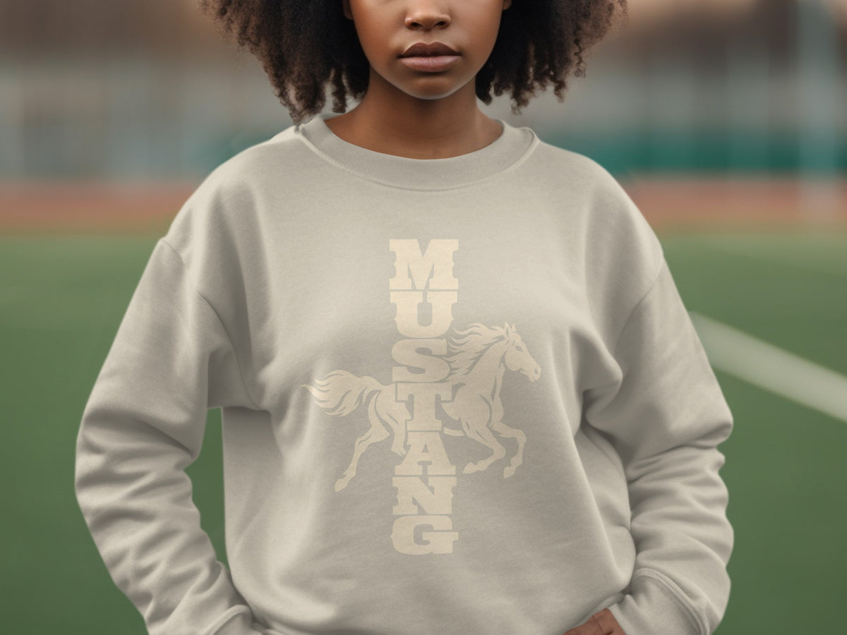 A woman with curly hair wearing a light beige sweatshirt printed with the word Mustang and a horse graphic.
