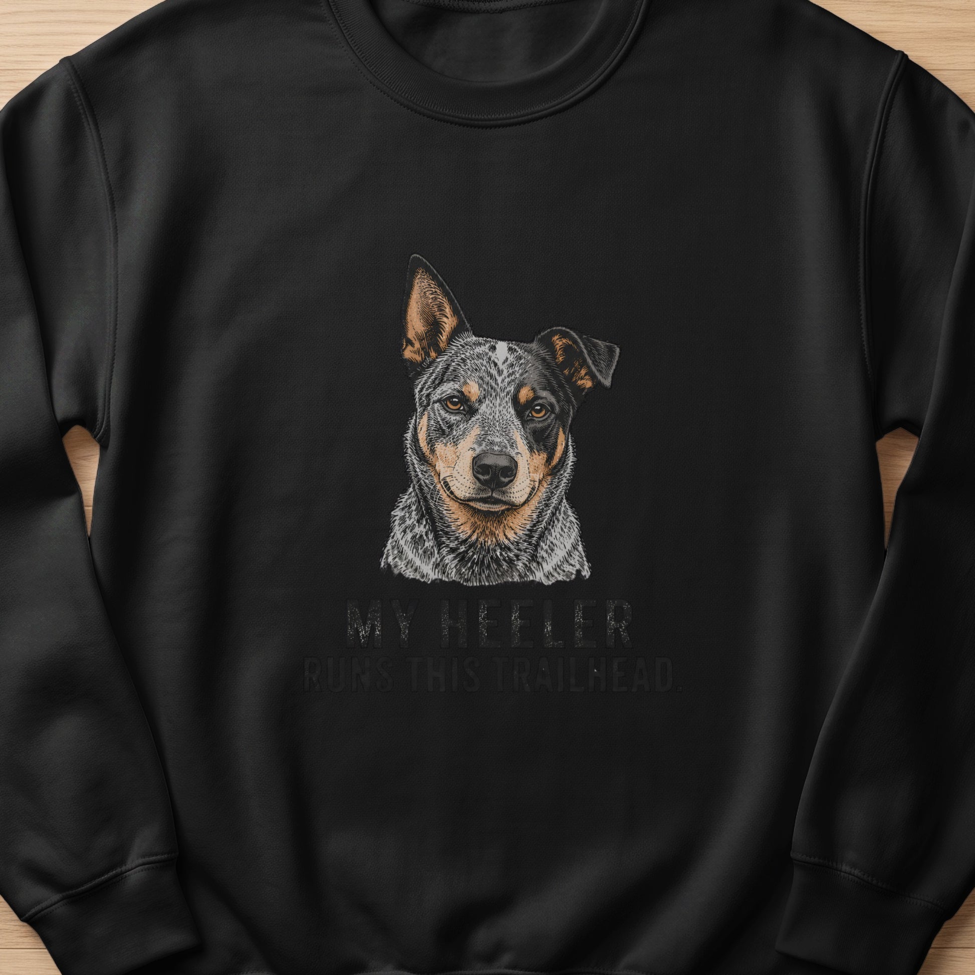 Black sweatshirt with an illustration of a heeler dog and text "MY HEELER RUNS THIS TRAILHEAD".