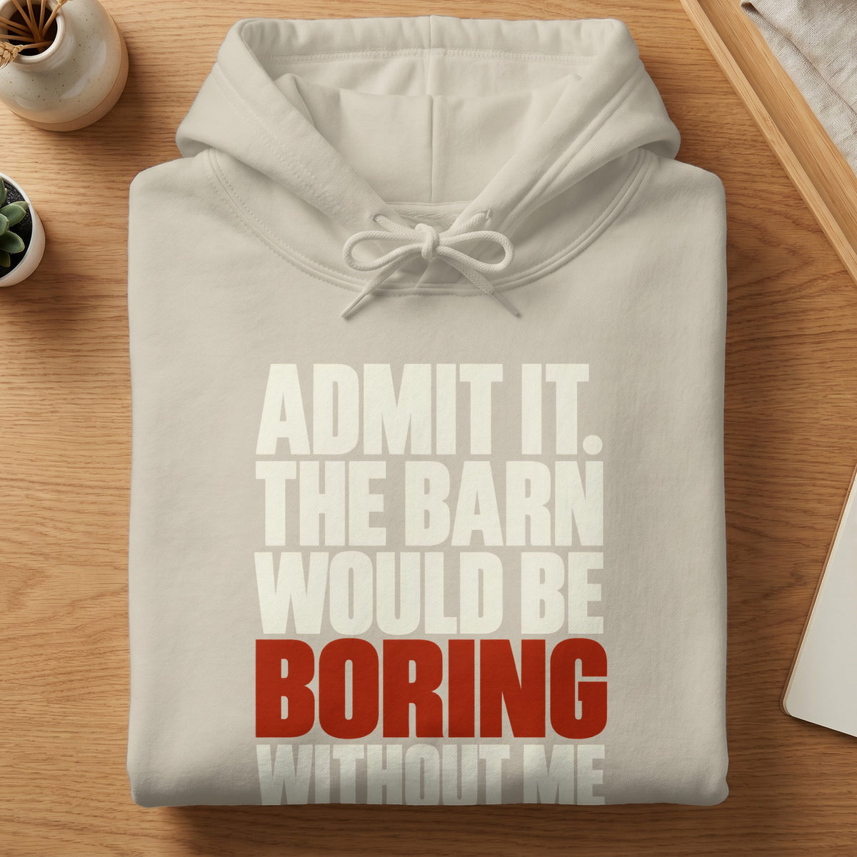 A folded cream-colored hooded sweatshirt with the text "ADMIT IT. THE BARN WOULD BE BORING WITHOUT ME."