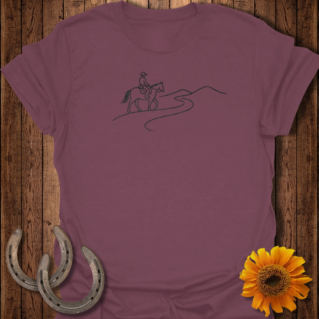 Burgundy t-shirt with a minimalist line drawing of a cowboy on horseback on a mountain path.