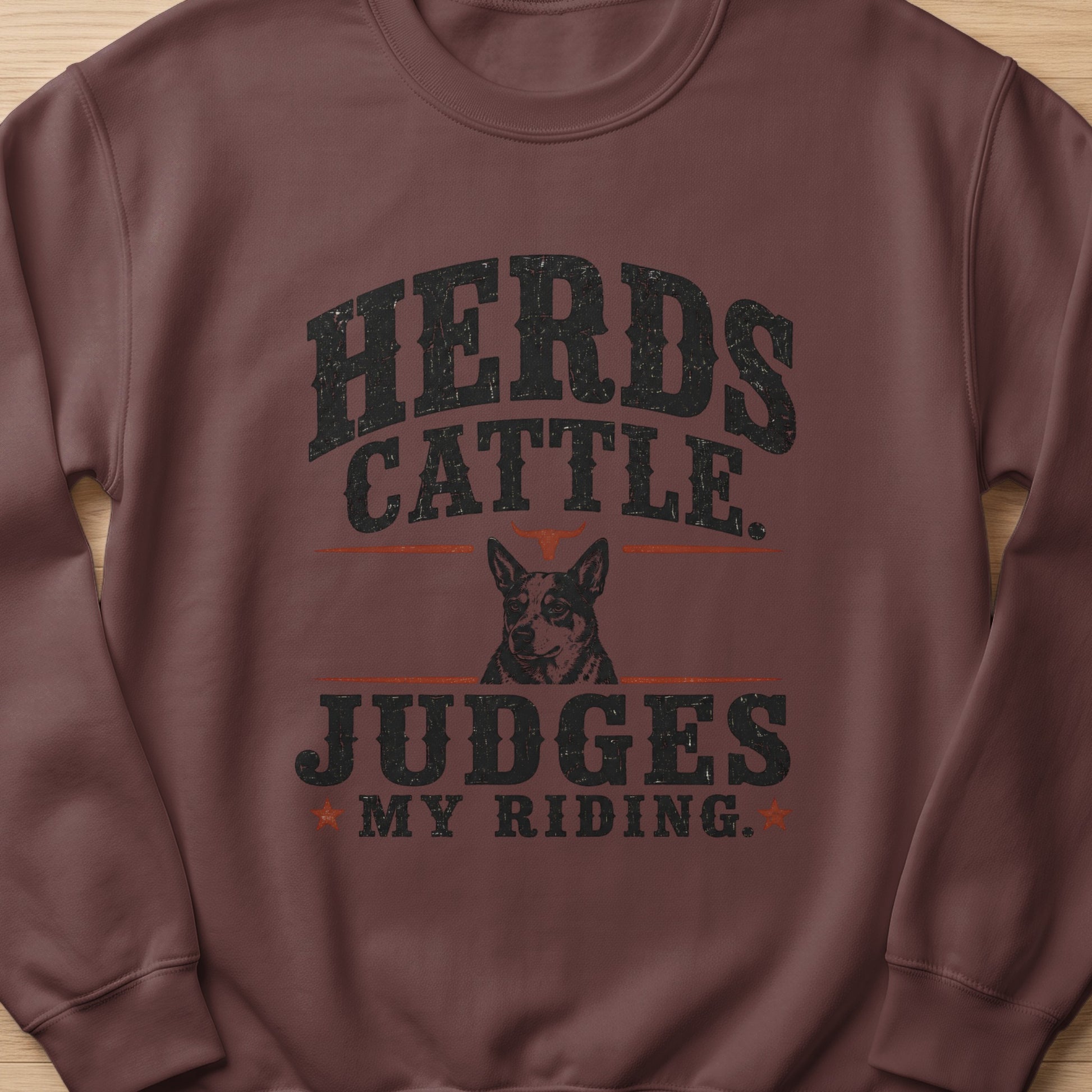 Brown crewneck sweatshirt with distressed "Herds Cattle. Judges My Riding." text and dog graphic.