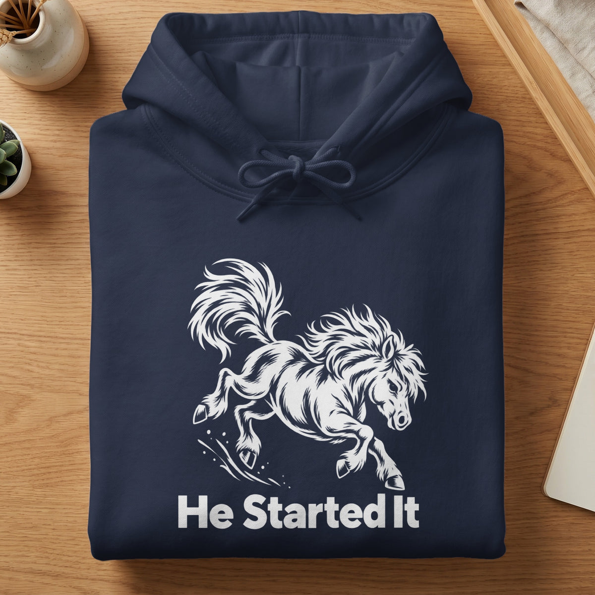 Folded navy blue hoodie with a white graphic of a running horse and the text He Started It.