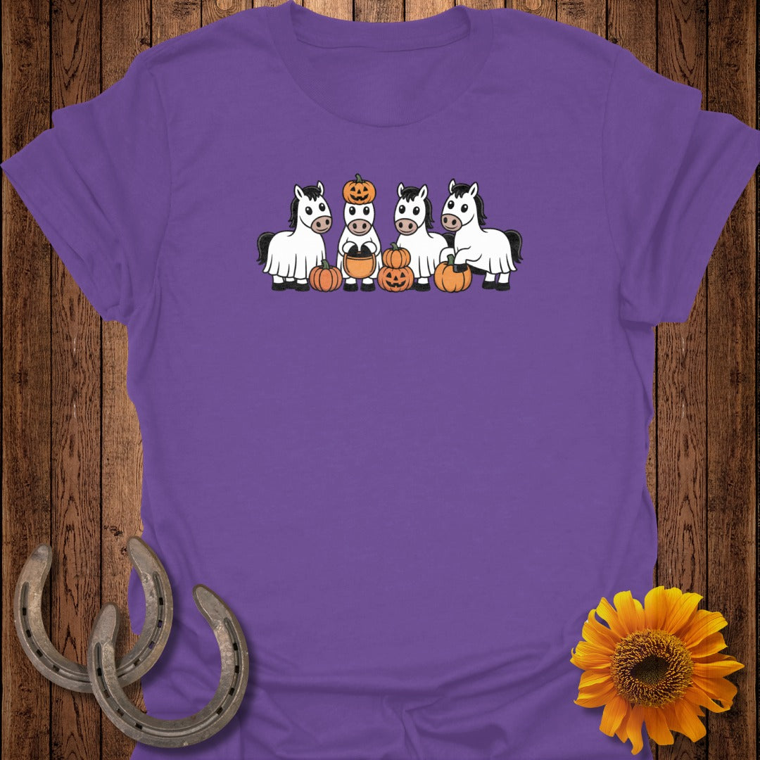 Four cartoon horses in ghost costumes with pumpkins surround them on a purple shirt.